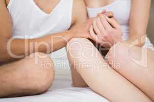 Couple holding hand while sitting on bed