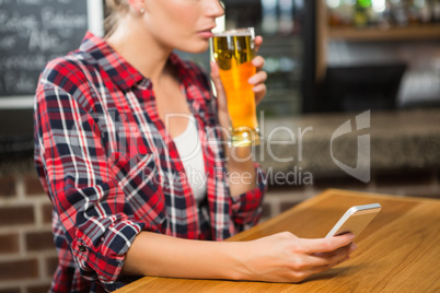 Pretty woman having a beer and looking at smartphone