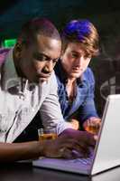 Two men having whiskey and using laptop at bar counter