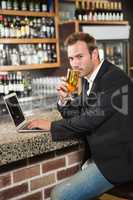 Handsome man using laptop computer and drinking a beer