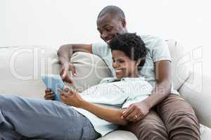 Pregnant couple using digital tablet on sofa