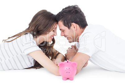 Happy couple lying on the floor with piggy bank