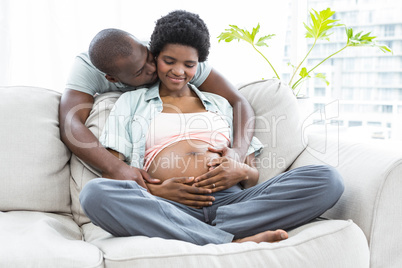 Man embracing and kissing pregnant woman from behind