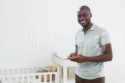 Smiling man standing next to a cradle and text messaging on mobi