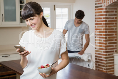 Woman using mobile phone while having breakfast cereals