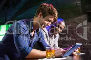 Two men using digital table while having whiskey at bar counter