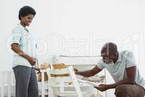 Pregnant woman looking at man fixing a baby chair