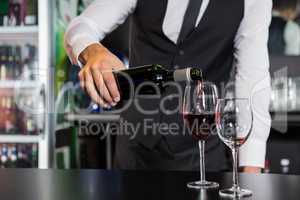 Mid section of bartender pouring red wine in a glass
