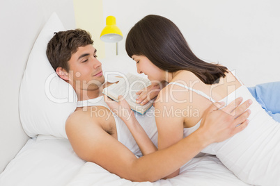 Woman lying on man and reading novel on bed