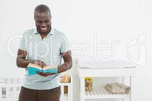 Smiling man standing in front of a cradle and reading a book