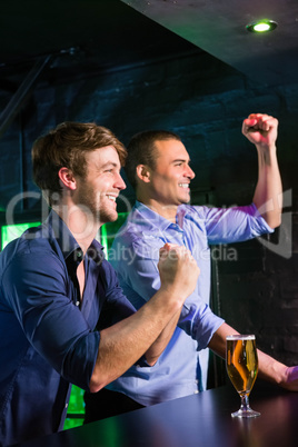 Two happy men raising their fist while having beer at bar counte
