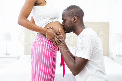 Man kissing pregnant womans belly in bedroom