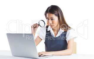 Businesswoman looking through magnifying glass and using laptop