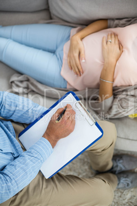 Doctor writing on clipboard while consulting pregnant woman