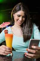 Beautiful woman typing a text message while having cocktail