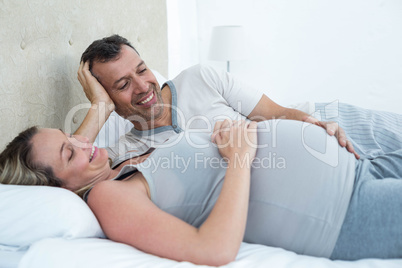 Expecting couple lying on bed and chatting