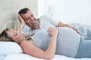 Expecting couple lying on bed and chatting