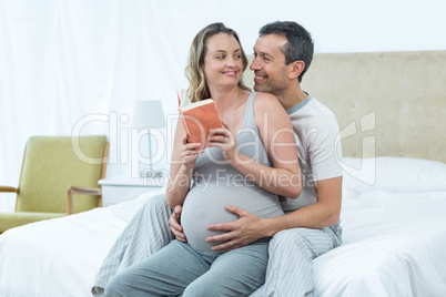 Expecting couple sitting on bed