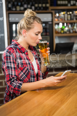 Pretty woman having a beer and looking at smartphone