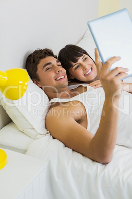 Couple using digital tablet on bed