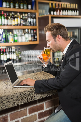 Handsome man using laptop computer and drinking a beer