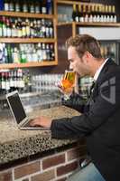 Handsome man using laptop computer and drinking a beer
