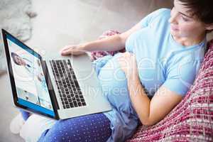 Composite image of pregnant woman using laptop at home
