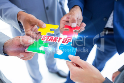 Start up against business colleagues holding piece of puzzle