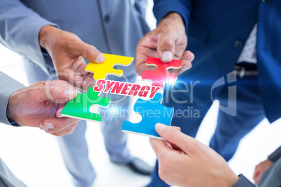 Synergy against business colleagues holding piece of puzzle