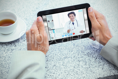 Composite image of businessman holding small tablet at table