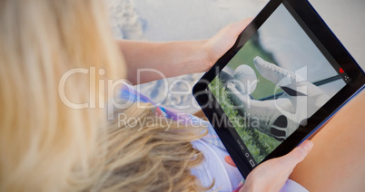 Composite image of woman sitting on beach in deck chair using ta