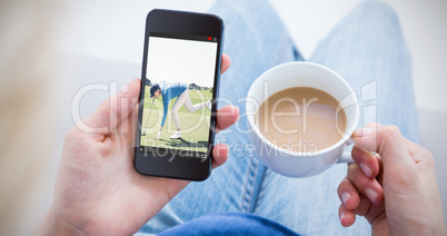 Composite image of woman using her mobile phone and holding cup