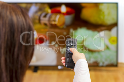 Young woman sitting on sofa holding tv remote and surfing progra