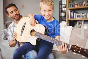 Happy man teaching guitar to son at home