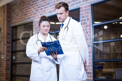 Two doctors looking at clipboard and discussing near library