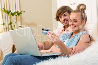 Cute couple using laptop to do online shopping sitting on the co