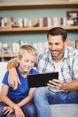 Smiling father and son using digital tablet while sitting on sof