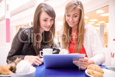 Women using digital tablet while having coffee and snacks