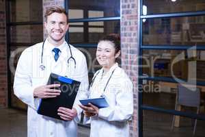 Portrait of doctors standing near library with clipboard and dig