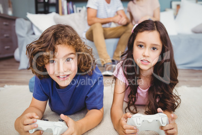 Siblings with remote playing video games on carpet