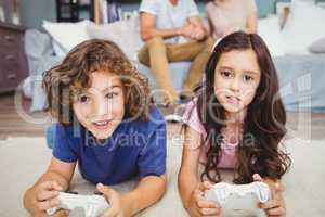 Siblings with remote playing video games on carpet
