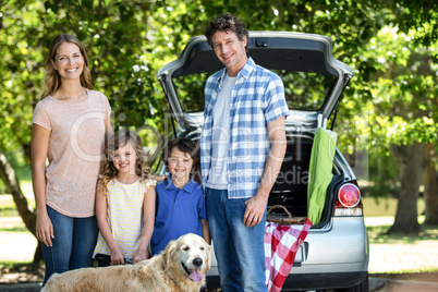 Smiling family standing in front of a car