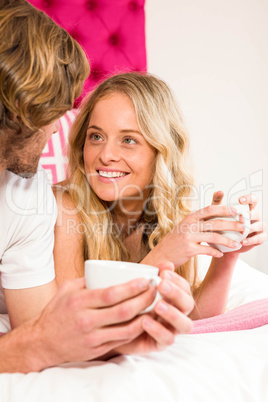 Cute couple relaxing on their bed and having coffee