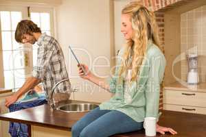 Pretty blonde using tablet while boyfriend ironing a shirt