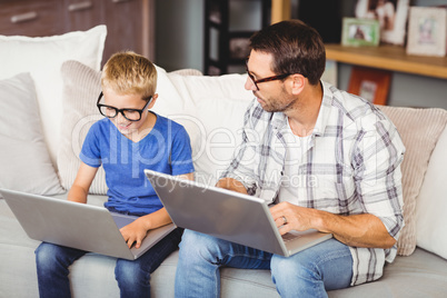 Father and son wearing eyeglasses while working on laptop