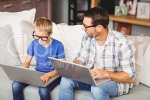 Father and son wearing eyeglasses while working on laptop