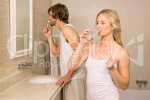 Blonde woman taking a pill with her boyfriend brushing his teeth