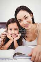 Portrait of happy mother and daughter with book on bed