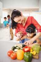 Happy woman teaching daughter to cut vegetables