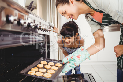 Mother and daughter placing cookies in oven